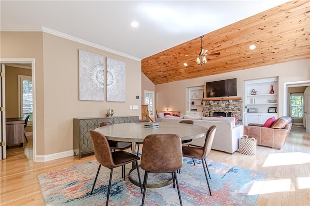 dining space with a wealth of natural light, a stone fireplace, built in shelves, and light wood-type flooring