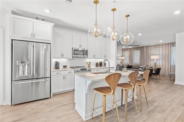 kitchen with a kitchen island with sink, white cabinets, sink, decorative light fixtures, and stainless steel appliances