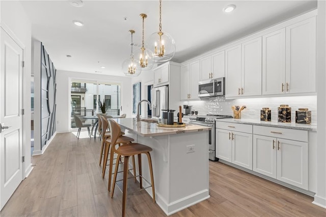 kitchen with hanging light fixtures, appliances with stainless steel finishes, a center island with sink, white cabinets, and light wood-type flooring