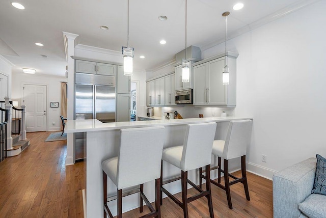 kitchen featuring pendant lighting, ornamental molding, a kitchen bar, wood-type flooring, and kitchen peninsula