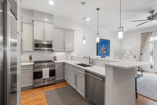 kitchen featuring a ceiling fan, a peninsula, gray cabinets, a sink, and premium appliances