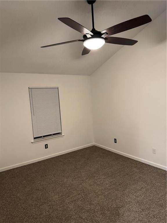 spare room with dark carpet, baseboards, ceiling fan, and lofted ceiling