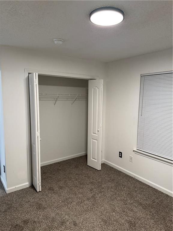 unfurnished bedroom featuring baseboards, a closet, dark carpet, and a textured ceiling