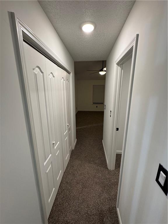 corridor with baseboards, dark carpet, and a textured ceiling