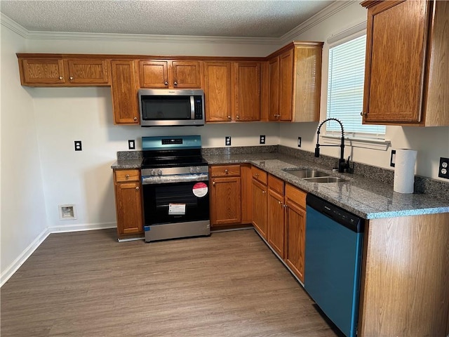 kitchen with a sink, appliances with stainless steel finishes, brown cabinetry, and light wood-style flooring