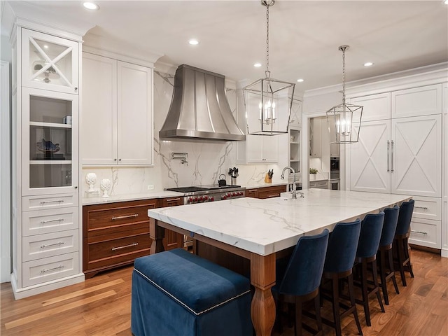 kitchen with white cabinets, a breakfast bar area, custom range hood, and hardwood / wood-style flooring