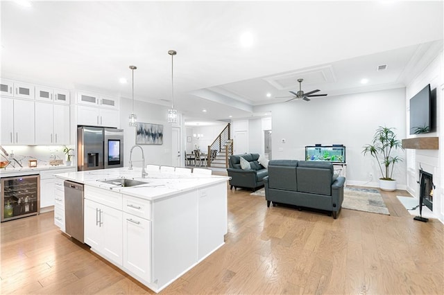 kitchen with beverage cooler, white cabinets, stainless steel appliances, an island with sink, and sink