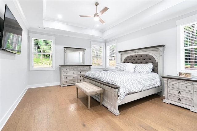 bedroom featuring a raised ceiling, ceiling fan, light hardwood / wood-style floors, and multiple windows