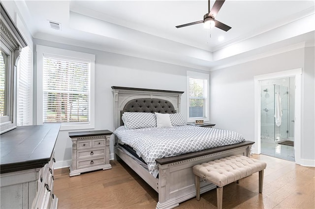 bedroom featuring ensuite bathroom, a raised ceiling, ceiling fan, and multiple windows