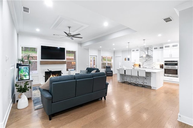 living room with light wood-type flooring, crown molding, a fireplace, ceiling fan, and sink