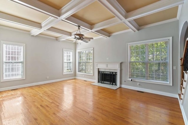 unfurnished living room with a wealth of natural light, coffered ceiling, a tiled fireplace, and light wood-type flooring