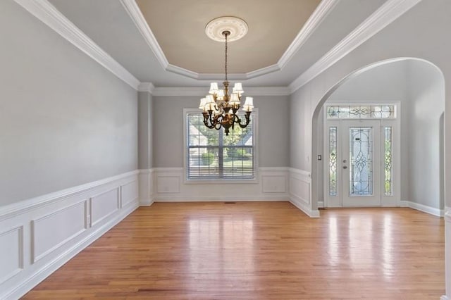 foyer featuring crown molding, a notable chandelier, light wood-type flooring, and a raised ceiling