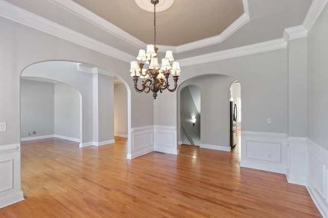 unfurnished dining area with ornamental molding, a chandelier, light wood-type flooring, and a raised ceiling