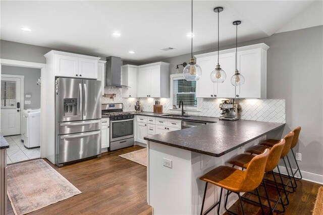 kitchen with pendant lighting, white cabinets, stainless steel appliances, and wall chimney range hood