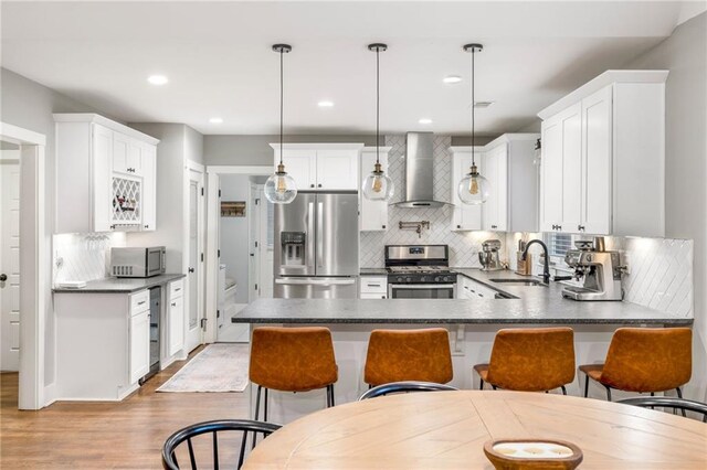 kitchen with sink, decorative light fixtures, stainless steel appliances, and wall chimney exhaust hood