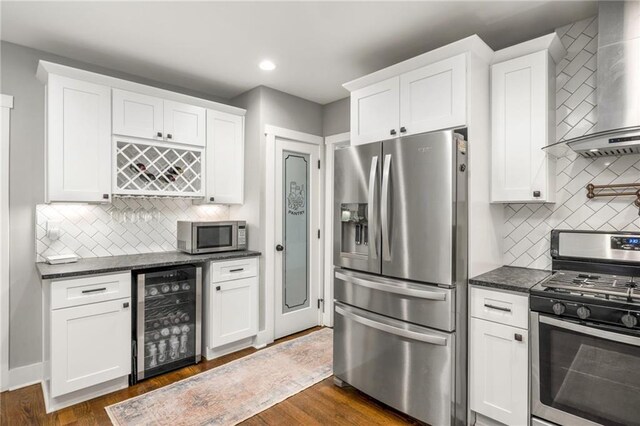 kitchen with wall chimney exhaust hood, appliances with stainless steel finishes, beverage cooler, and white cabinets