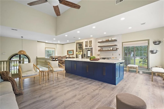 kitchen with light hardwood / wood-style flooring, blue cabinetry, stainless steel fridge with ice dispenser, ceiling fan, and a towering ceiling