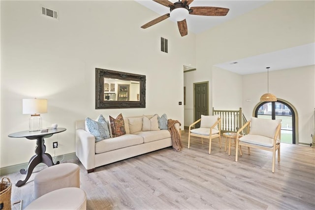 living room with ceiling fan, a towering ceiling, and light hardwood / wood-style floors