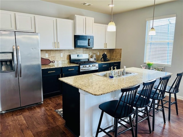 kitchen featuring hanging light fixtures, white cabinetry, appliances with stainless steel finishes, and a kitchen island with sink