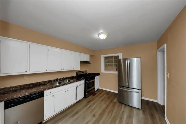 kitchen with white cabinetry, sink, dark stone counters, stainless steel appliances, and light wood-type flooring