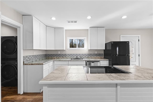 kitchen featuring sink, dark wood-type flooring, stacked washer / dryer, white cabinets, and black fridge