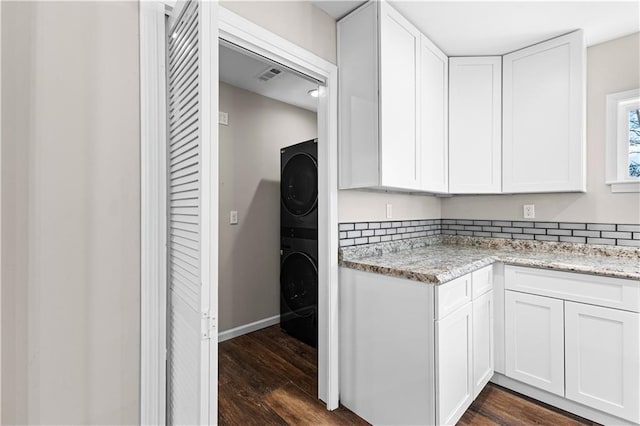 kitchen featuring dark wood-type flooring, light stone countertops, white cabinets, and stacked washer / dryer