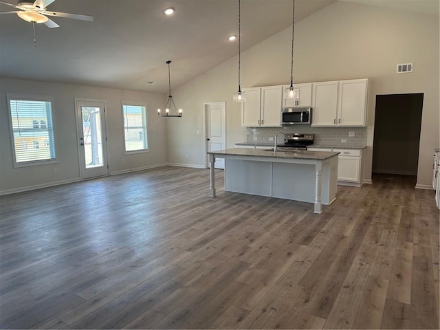 kitchen featuring white cabinetry, stainless steel appliances, dark wood-type flooring, high vaulted ceiling, and a center island with sink