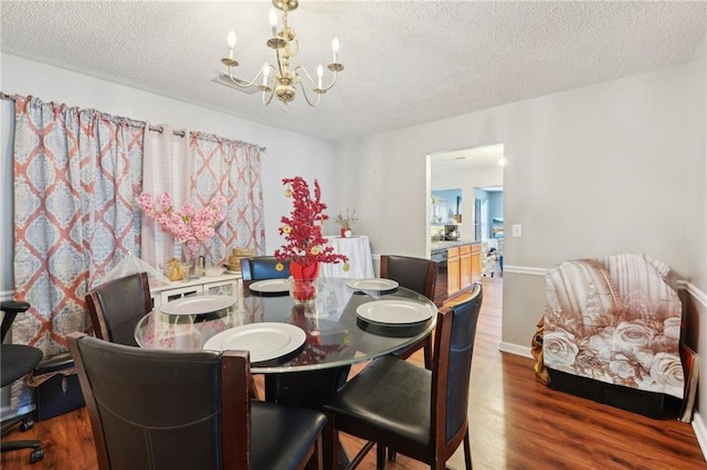 dining area featuring a chandelier, a textured ceiling, wood finished floors, and baseboards