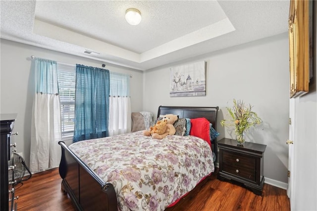 bedroom with a tray ceiling, dark wood-type flooring, a textured ceiling, and baseboards