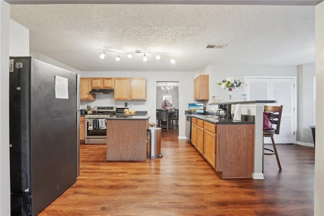kitchen with stainless steel range with gas stovetop, dark countertops, light wood finished floors, a kitchen breakfast bar, and a textured ceiling