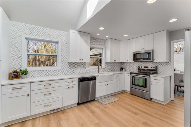 kitchen featuring stainless steel appliances, white cabinetry, sink, and light hardwood / wood-style floors