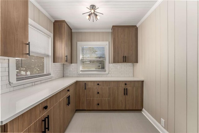 kitchen featuring brown cabinets, crown molding, light countertops, and backsplash