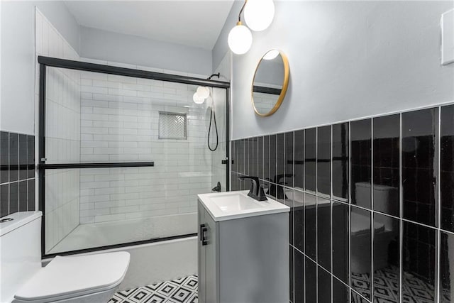 full bath featuring bath / shower combo with glass door, wainscoting, toilet, vanity, and tile walls