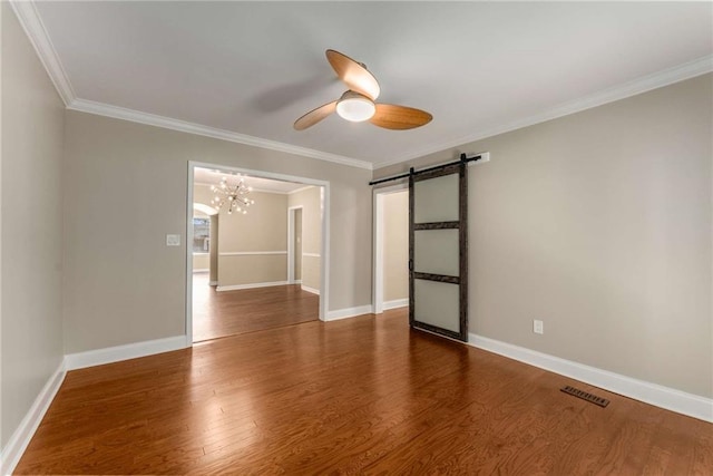 empty room featuring a barn door, visible vents, ornamental molding, wood finished floors, and ceiling fan with notable chandelier