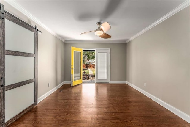 spare room with baseboards, a barn door, wood finished floors, and crown molding