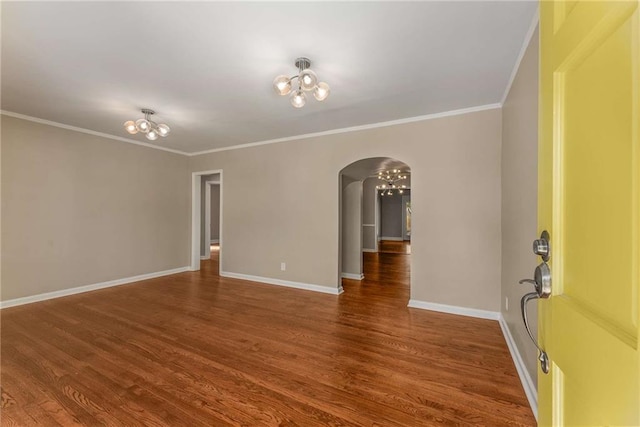 empty room featuring baseboards, crown molding, arched walkways, and wood finished floors