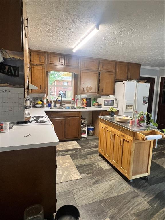 2194 Meadow Dr, Snellville, GA 30078 - kitchen with white appliances, a sink, a textured ceiling, brown cabinetry, and dark floors