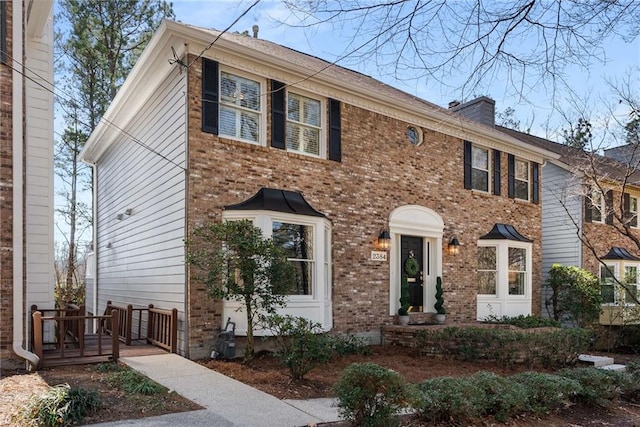 colonial inspired home with brick siding and a chimney