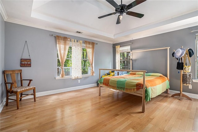 bedroom with a tray ceiling, light wood-style flooring, baseboards, ornamental molding, and ceiling fan
