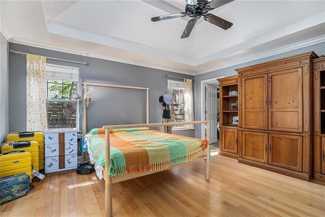bedroom with a tray ceiling, light wood-style floors, and a ceiling fan