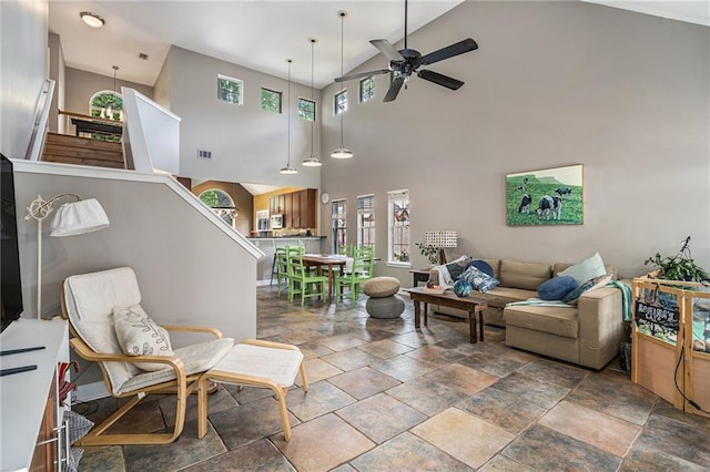 living room with stone tile flooring, ceiling fan, a towering ceiling, and plenty of natural light