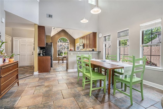 dining room with baseboards, healthy amount of natural light, a high ceiling, and light stone finish floors