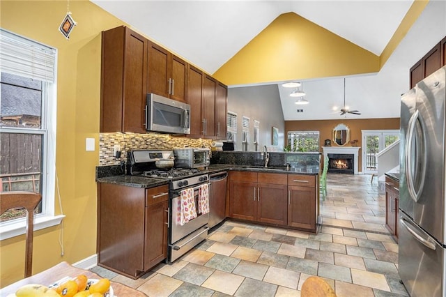 kitchen with appliances with stainless steel finishes, a sink, a peninsula, a warm lit fireplace, and tasteful backsplash