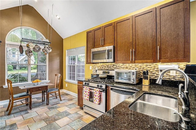 kitchen with appliances with stainless steel finishes, a sink, backsplash, baseboards, and light stone finish flooring