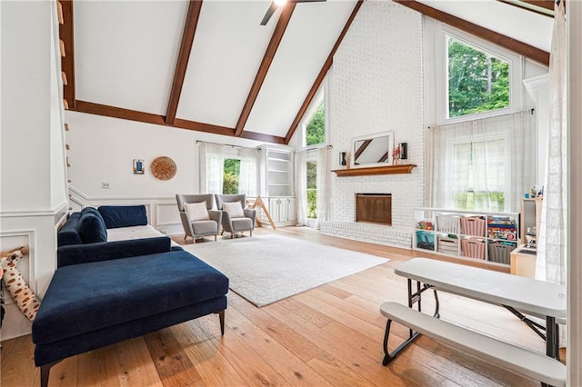 living room with high vaulted ceiling, a fireplace, beamed ceiling, hardwood / wood-style flooring, and wainscoting