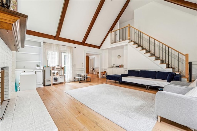 living area with high vaulted ceiling, light wood-style floors, stairway, beamed ceiling, and a fireplace