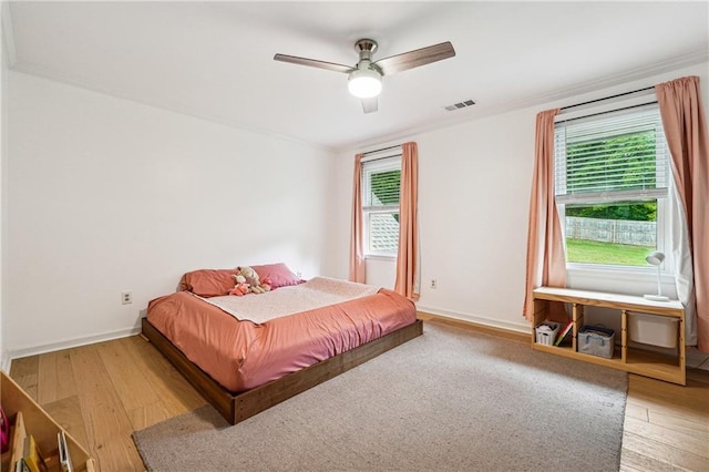 bedroom featuring multiple windows, wood finished floors, baseboards, and crown molding