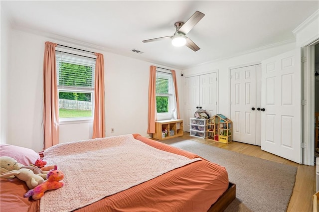 bedroom featuring multiple closets, multiple windows, wood finished floors, ceiling fan, and crown molding