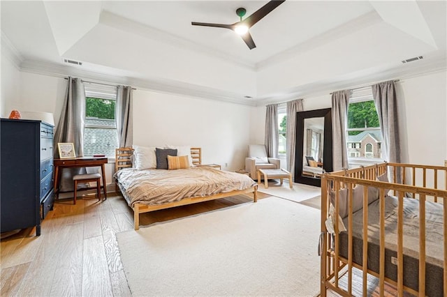 bedroom featuring a tray ceiling, multiple windows, light wood-style floors, ornamental molding, and ceiling fan