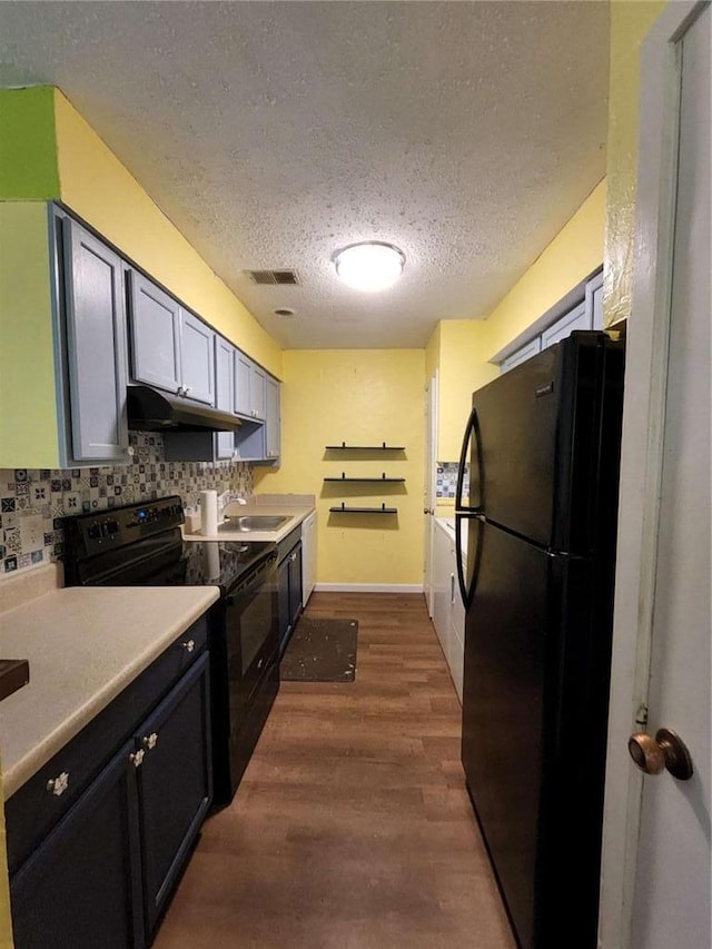 kitchen with tasteful backsplash, wood-type flooring, sink, black appliances, and a textured ceiling